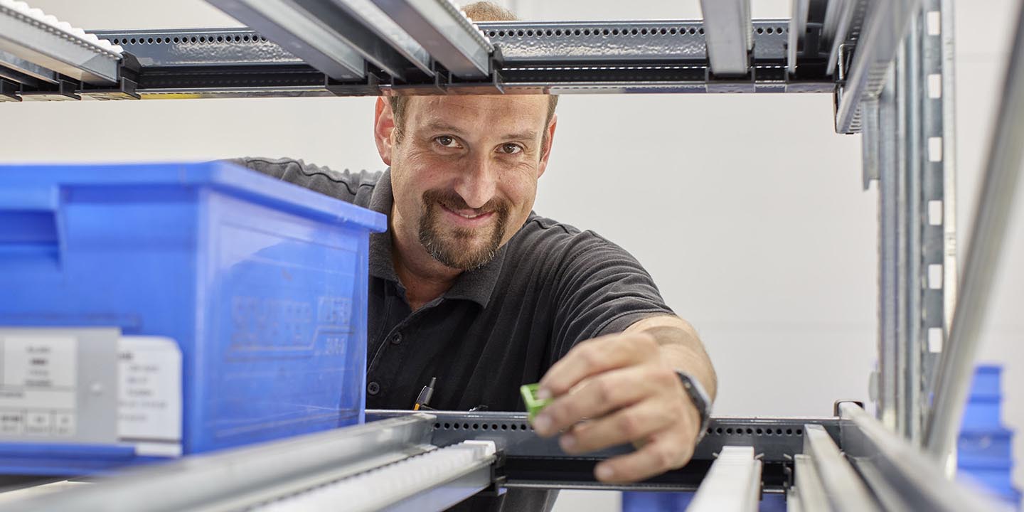 Arbeiter hantiert mit Automatisierungskomponenten für die Elektrotechnik in einem Lagerregal