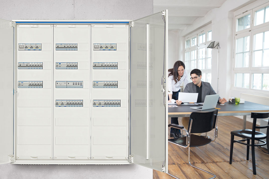 Blick in Büro mit Hager Feldverteiler mit 3 Feldern im Vordergrund und darin installierten elektrischen/elektronischen Baugruppen