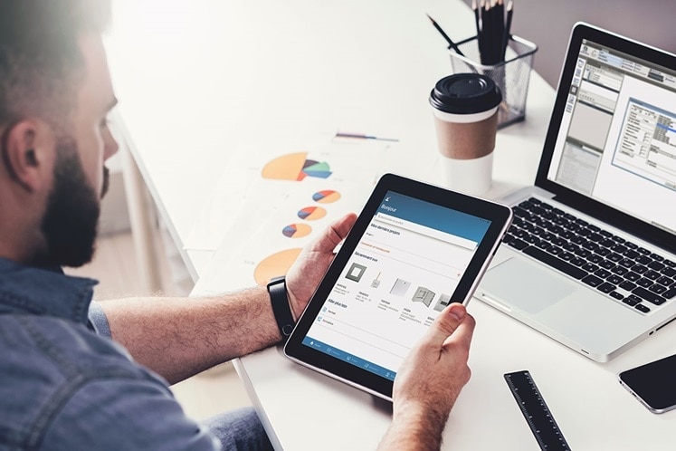 Persona utilizando una tableta con aplicación de domótica frente a una computadora portátil y gráficos impresos en el escritorio