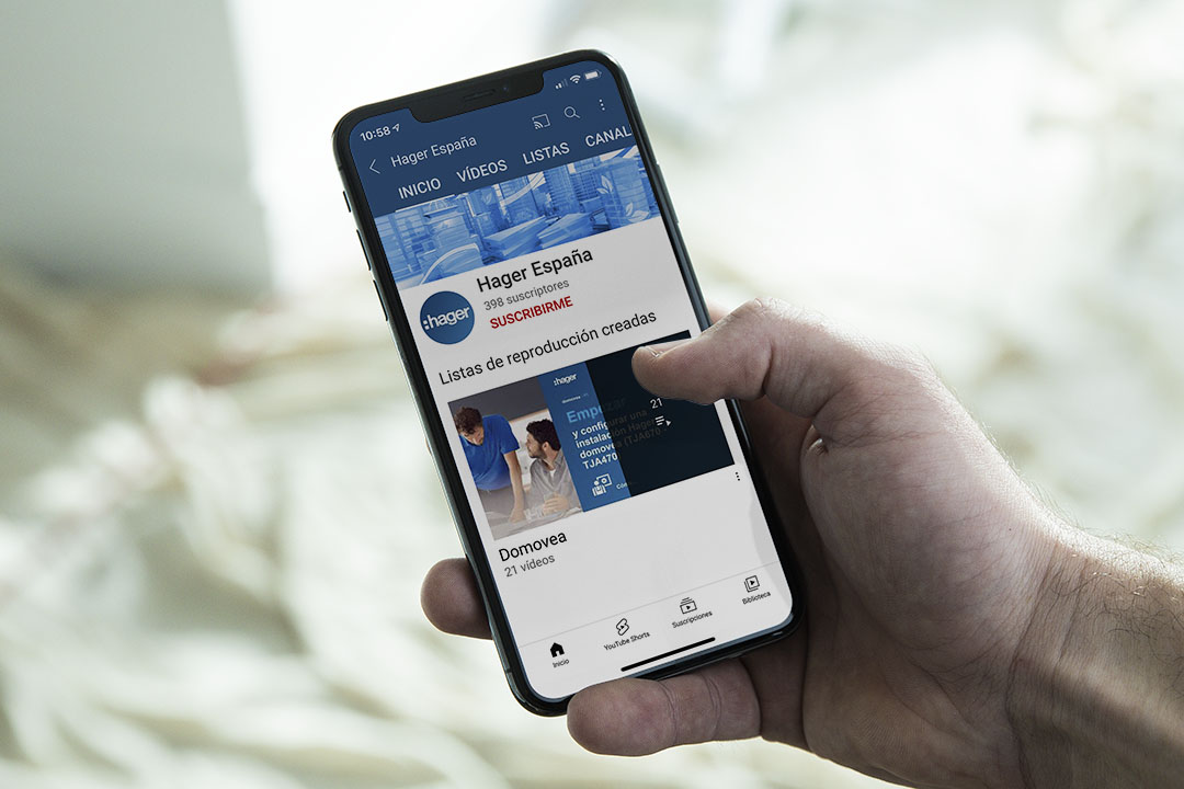 Persona sosteniendo un teléfono inteligente mostrando el canal de YouTube de Hager España con listas de reproducción de videos