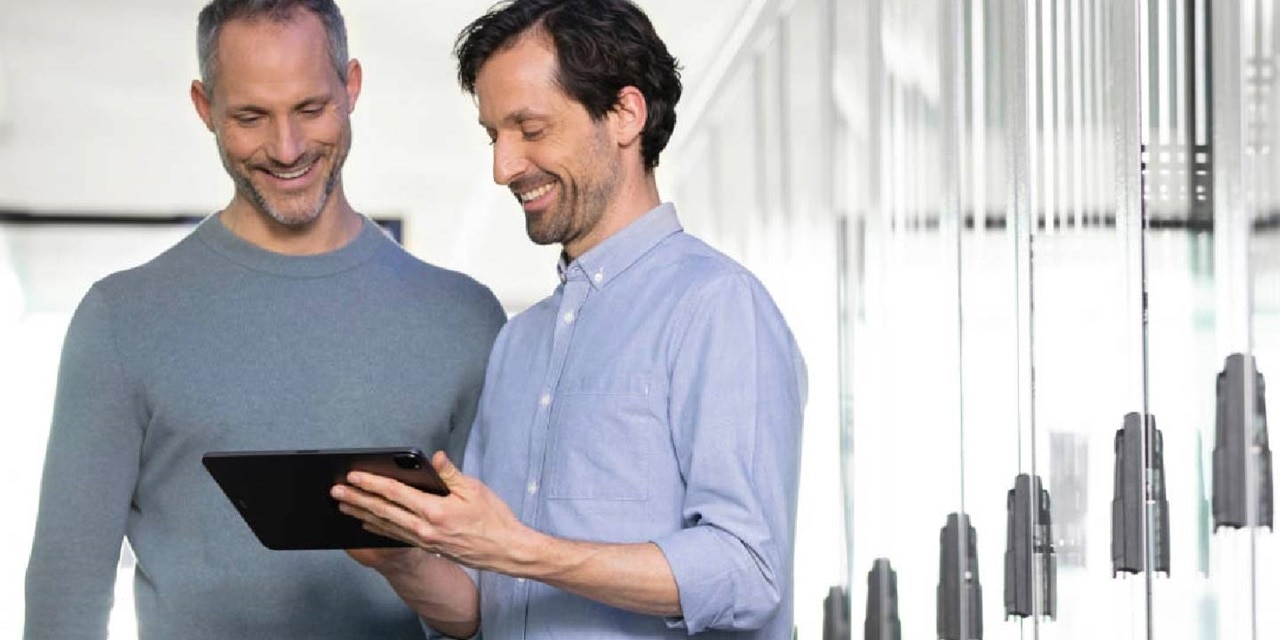 Two professionals smiling and looking at a tablet in a modern office environment